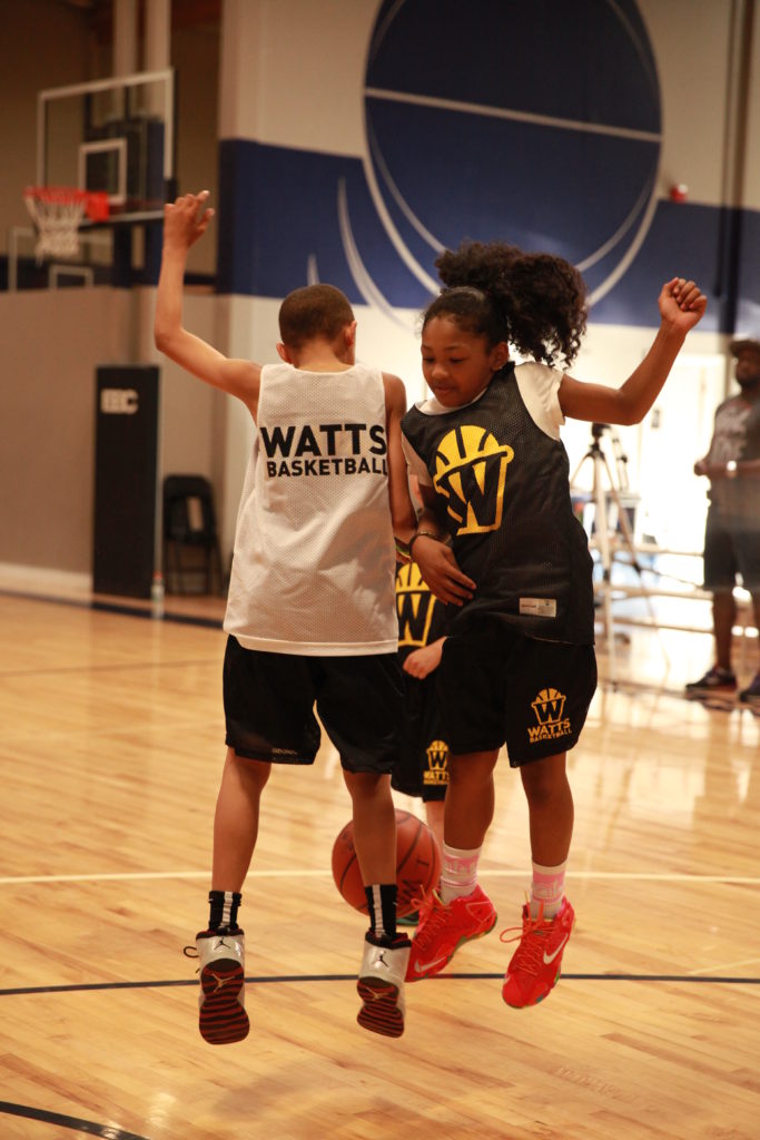 Two kids jumping for basketball in gym