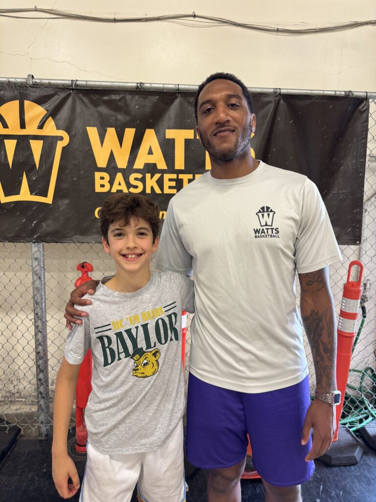 Boy and coach posing by Watts Basketball banner